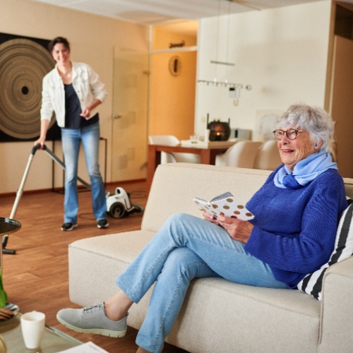 Medewerker van DNZT met tablet aan de deur bij een oudere bewoner in appartementencomplex.